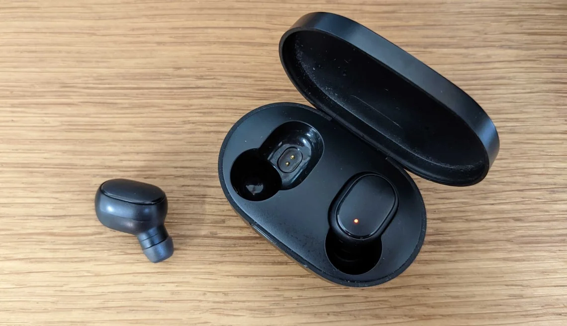 Zwei schwarze True-Wireless-Ohrhörer liegen neben ihrem geöffneten Ladecase auf einem Holztisch.