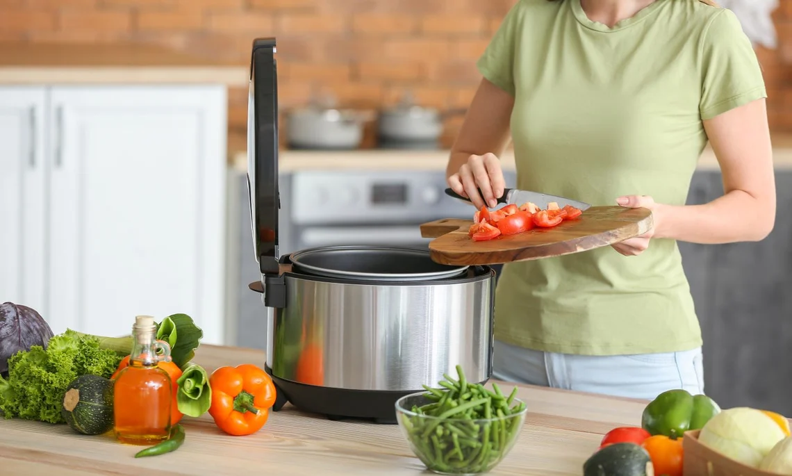 Frau gibt frische Tomaten in den Topf eines Multikochers.