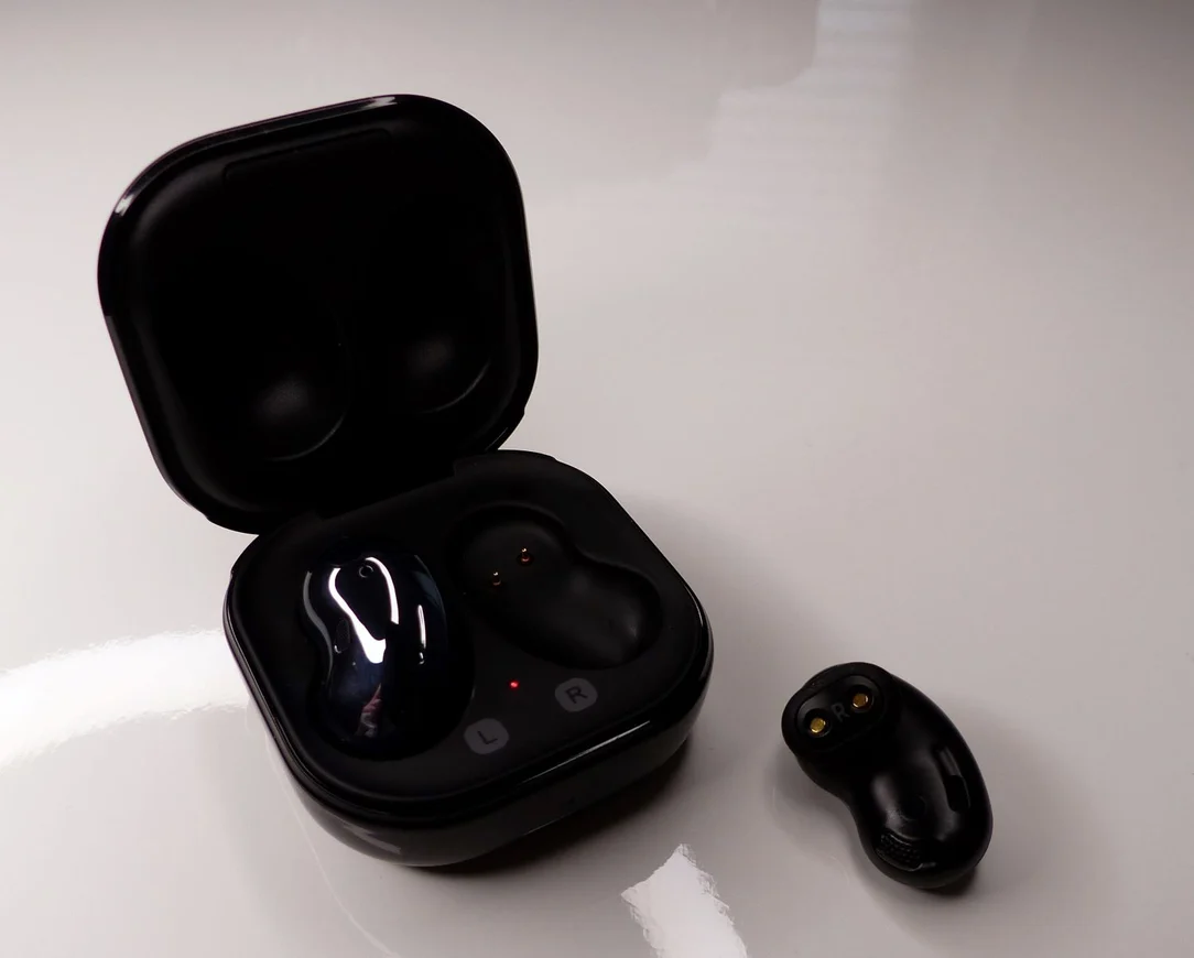 Bohnenförmige In-Ear-Kopfhörer ohne Silikonaufsatz liegen neben ihrem geöffneten Ladecase.